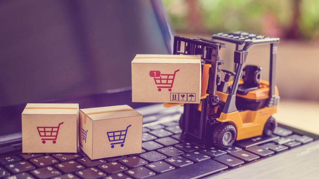 A close-up photo of a miniature yellow forklift moving a cardboard box on a laptop keyboard, representing Consolidation and DDP shipping services.