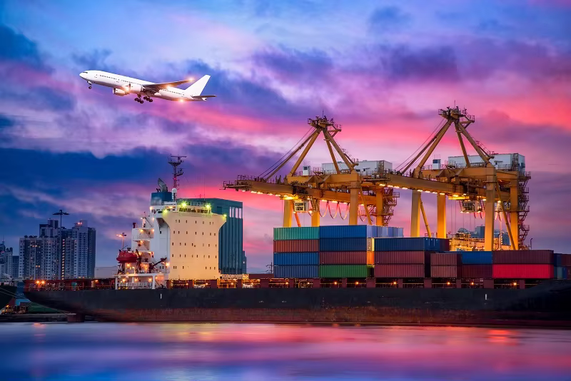 A twilight photo of a container port with a cargo ship, yellow cranes, and a flying airplane, representing multimodal logistics for Consolidation and DDP.