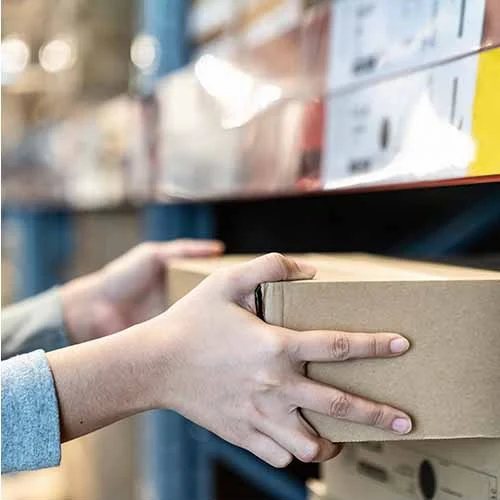 Close-up of hands handling a cardboard box on a warehouse shelf, representing the process of receiving small trial orders from China.
